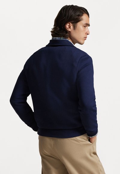 Sweatshirt azul marinho com textura suave, detalhe na gola e bainha com nervuras. Usado com calças cáqui, apresentando um design casual e ajustado.