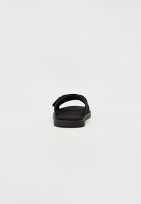 Svart sandal med myk stoffoverdel, justerbar stropp, flat gummisåle og teksturert fotseng. Minimalistisk design med en enkel silhuett.