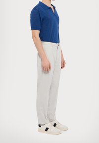 Polo azzurro a maniche corte con un motivo testurizzato, abbinato a pantaloni grigi chiari e sneakers bianche con dettagli neri.