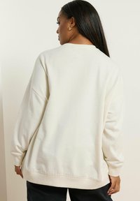 Sudadera oversize de color beige claro con una textura suave, puños y dobladillo con canalé. Presenta un cuello redondo y un ajuste relajado, ideal para usar en capas.