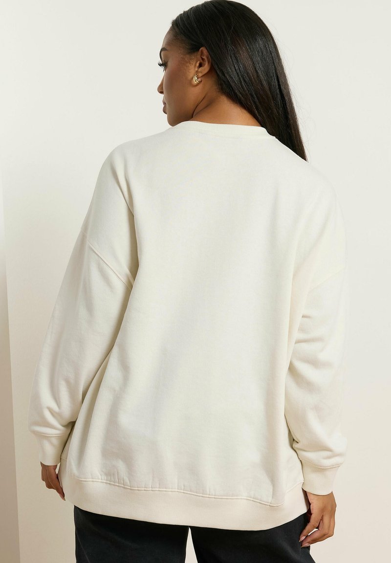 Sudadera oversize de color beige claro con una textura suave, puños y dobladillo con canalé. Presenta un cuello redondo y un ajuste relajado, ideal para usar en capas.