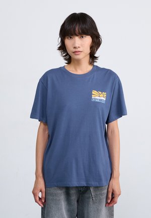T-shirt en coton bleu à manches courtes, avec un design graphique représentant un soleil et du texte sur la zone gauche de la poitrine. Coupe décontractée et texture douce.