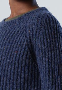 Granatowy sweter z dzianiny o prążkowanej fakturze i wielokolorowymi plamkami, z okrągłym dekoltem i naszywką z logo na rękawie.