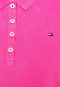 Een roze poloshirt van een gestructureerde stof, met een placket met twee knopen en een klein geborduurd logo in de onderste hoek.