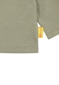 T-shirt verde olivo a maniche corte realizzato in cotone, con orlo cucito e un'etichetta del marchio gialla visibile sulla cucitura laterale.