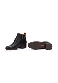 Stivaletti in pelle nera alla caviglia con cerniera laterale, tacco basso e impilato, texture liscia e suola in gomma con fantasia. Presentano un accento in pelle marrone sul tacco.