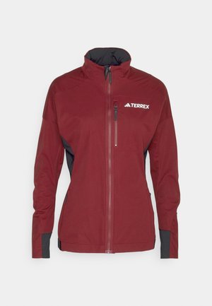 Bordeauxfarbene Softshell-Jacke mit schwarzen Akzenten, durchgehendem Reißverschluss, hohem Kragen, Reißverschlusstasche auf der Brust und Logo auf der linken Seite. Ergonomisches Design.