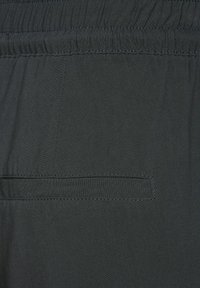 Svart tyg, elastisk midja, med en enda bakficka med en sydd klaff. Slät textur, mjukt fall, minimalistiska designelement.
