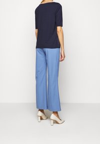 T-shirt bleu marine à manches courtes associé à un pantalon bleu clair. Le modèle porte des chaussures à talons beiges. Tissu lisse et coupe ample.