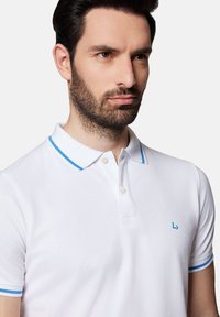 Biały polo z niebieskimi akcentami przy kołnierzyku i małym logo po lewej stronie piersi; wykonany z teksturowanej bawełnianej tkaniny z trzema guzikami przy rozwarciu.