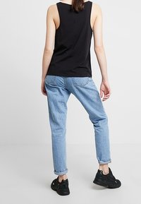 Musta ilmanhiha tank top, joka on yhdistetty vaaleansinisiin farkkuihin. Farkut ovat kääritty lahkeista, ja mustat lenkkarit viimeistelevät kokonaisuuden.