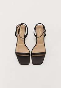 Sandales noires à brides avec un embout carré, dotées d'une finition mate, de fines brides et d'une semelle intérieure en cuir beige rembourrée. Logo de la marque sur la semelle intérieure.