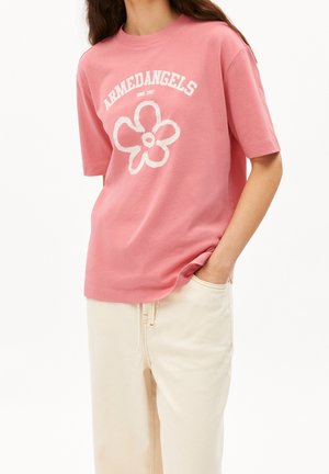 T-shirt en coton rose à coupe décontractée, avec un motif floral blanc et un logo textuel, assorti à un pantalon de couleur crème.