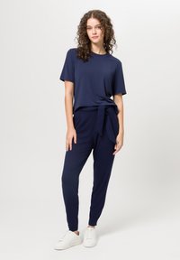 Námořnická modrá volná košile s krátkým rukávem, kombinovaná s námořnickými kalhotami se zavazovacím pasem, doplněná bílými teniskami. Hladký materiál.