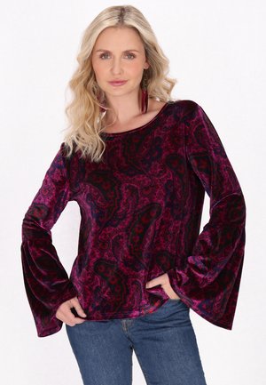 Top in velluto borgogna con motivo paisley, maniche a campana lunghe e scollatura ampia, abbinato a jeans blue. Tessuto morbido con finitura lucida.