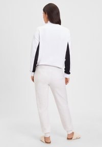 Witte sweatshirt met zwarte mouwaccenten, gecombineerd met lichtgrijze joggingbroek en beige slippers. Zacht, ontspannen pasvorm en geribbelde manchetten.