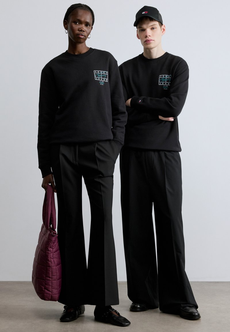 Black sweatshirts feature graphic designs on the front, paired with black trousers. A purple quilted bag is held by one model.