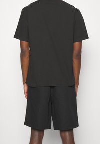 Černé tričko s krátkým rukávem a rovým lemem, spárované s černými šortkami. Oba kousky mají hladkou strukturu a jednoduchý design.