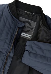 Tmavomodrá bomber bunda s prešívanou textúrou, rebrovaným golierom a manžetami, zapínaním na zips a štítkom s označením veľkosti 104. Hladká vnútorná podšívka.