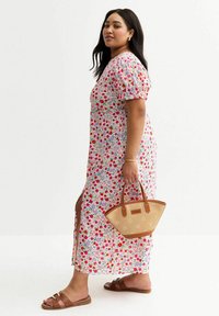 Abito maxi floreale con maniche a sbuffo, fiori multicolori su uno sfondo chiaro, spacco laterale. Abbinato a una borsa color tan e sandali marroni.