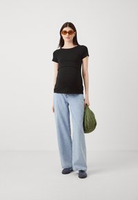 Črni kratki rokavič pritemnjen z svetlo modrimi širokimi hlačami. Model nosi zeleni prešiti nahrbtnik in nosi oranžne sončne očala.