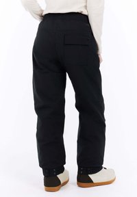 Zwarte broek met een relaxte pasvorm, voorzien van een elastische tailleband en een achterzak. Gecombineerd met lichtgekleurde, lage schoenen.