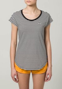 Camiseta de manga corta a rayas blancas y negras con escote redondo y pequeño logo en el pecho, combinada con pantalones cortos naranjas.