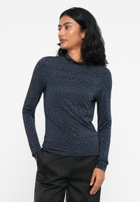 Langermet, tettsittende topp i mørkeblå med et subtilt leopardmønster. Myk, elastisk stoff med høy hals og buet sømdetalj.