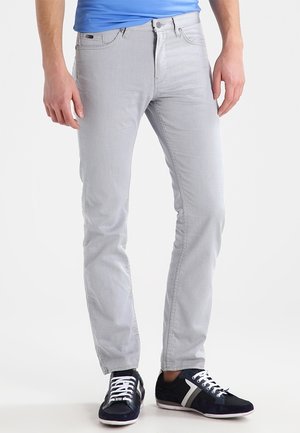 Jeans gris claro con un diseño ajustado, presentando un clásico cierre de botón y cremallera, combinados con zapatillas navy y una camisa azul.