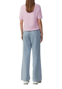 Jasnoróżowa, krótkosleeve'owa dzianinowa bluzka w połączeniu z jasnoniebieskimi spodniami z wysokim stanem i szerokimi nogawkami, charakteryzującymi się luźnym krojem i subtelną teksturą.
