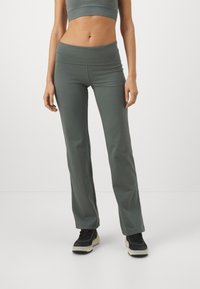 Lettvektige, elastiske grå leggings med høyt liv, flagrende design og jevn tekstur. Stylet med en kort T-skjorte og svarte joggesko.