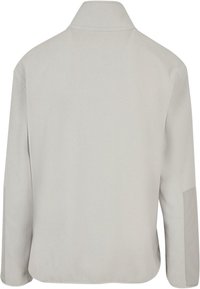 Vaaleanharmaa fleece-takki, jossa on korkea kaulus, pitkät hihat ja sileä pinta. Sisältää sivuaukot liikkumisen helpottamiseksi.