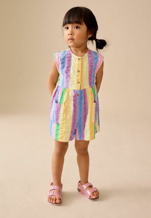 Bunter gestreifter Jumpsuit in Gelb, Lila, Grün und Pink, mit kurzen Ärmeln, rundem Ausschnitt, Knöpfen vorne und Taschen. Kombiniert mit pinkfarbenen Sandalen.