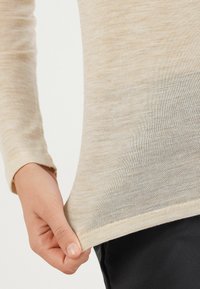 Beige Langarmoberteil aus leichtem, strukturiertem Stoff, das eine taillierte Passform hat und einen subtilen Farbverlauf von hell zu dunklerem Beige am Saum aufweist.
