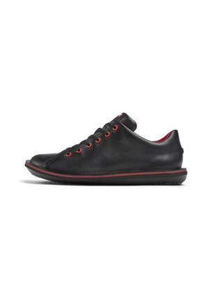 Black leather sneakers with red eyelets and trim, featuring a rounded toe and textured upper, set on a black rubber sole.