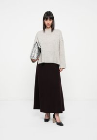 Gray knitted sweater, burgundy maxi skirt, and black high-heeled shoes; holding a metallic snakeskin-patterned clutch.