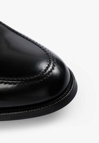 Punta de zapato de cuero negro con un acabado suave, costura detallada a lo largo del borde y una forma redondeada. La suela tiene un diseño texturizado para mayor agarre.