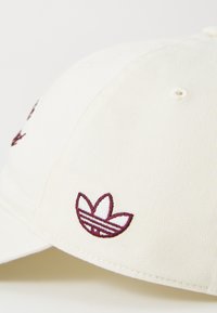 Hvit stoff baseballcaps med en liten bordeaux brodert Adidas trefoil-logo på sidepanelet.