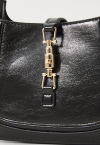 Borsa a mano sintetica nera con finitura lucida, dotata di chiusura e accessori in tono oro, forma strutturata e tracolla in pelle.