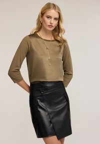 Olivově zelený top s tříčtvrtečními rukávy, spárovaný s černou sukní z umělé kůže s překlady, patentkami a bočními kapsami. Zlatý řetízkový náhrdelník.