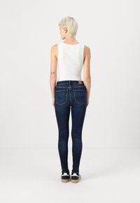 Sötét farmer skinny farmernadrág, közepes derékkal, öt zsebbel és kontrasztos varrással. Fehér trikóval és sportcipővel párosítva.