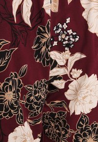 Burgundy fabric with large floral patterns in beige and black, featuring distinct leaves and flower details, creating a textured appearance.