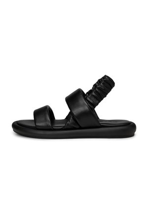 Schwarze flache Sandale mit zwei breiten vorderen Riemen und einem gerafften elastischen hinteren Riemen auf einer dicken Sohle, Seitenansicht vor weißem Hintergrund.