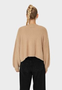 Beige flauschiger, verkürzter Pullover mit tief sitzenden Schultern, kombiniert mit hochgeschnittenen schwarzen Jeans. Weiche Textur und lockere Passform sind von hinten gut zu erkennen.