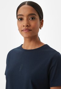 Navyblaue Baumwoll-T-Shirt mit rundem Halsauschnitt, kurzen Ärmeln und dezent gesticktem Logo-Detail auf der Vorderseite. Glatte Textur.