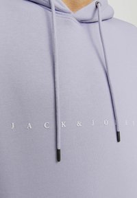 Šviesiai violetinė hoodie su kengūros kišene, raišteliais juodais galiukais ir balta tekstu "JACK & JONES" per priekinę dalį.