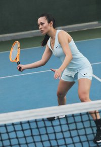 Conjunto atlético de color azul claro con escote en V y pantalones cortos, que presenta un logo de Nike en negro. Jugador sosteniendo una raqueta de tenis naranja, concentrado en el juego.