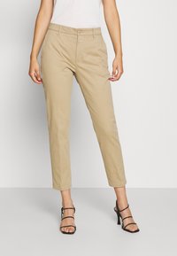 Beżowe chinosy o prostym kroju, z przednimi kieszeniami, wykonane z bawełny, z pojedynczym zapięciem na guzik, w zestawie z czarnymi sandałami na wysokim obcasie z paskami.