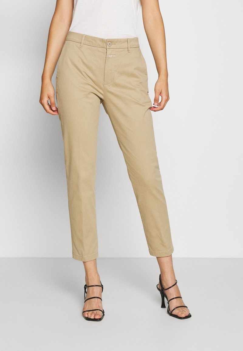 Beżowe chinosy o prostym kroju, z przednimi kieszeniami, wykonane z bawełny, z pojedynczym zapięciem na guzik, w zestawie z czarnymi sandałami na wysokim obcasie z paskami.