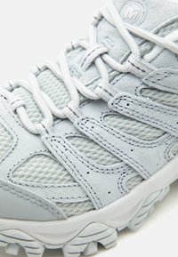 Chaussure de randonnée gris clair avec mesh texturé et panneaux en suède, coutures détaillées, semelle épaisse en caoutchouc et lacets blancs croisés.